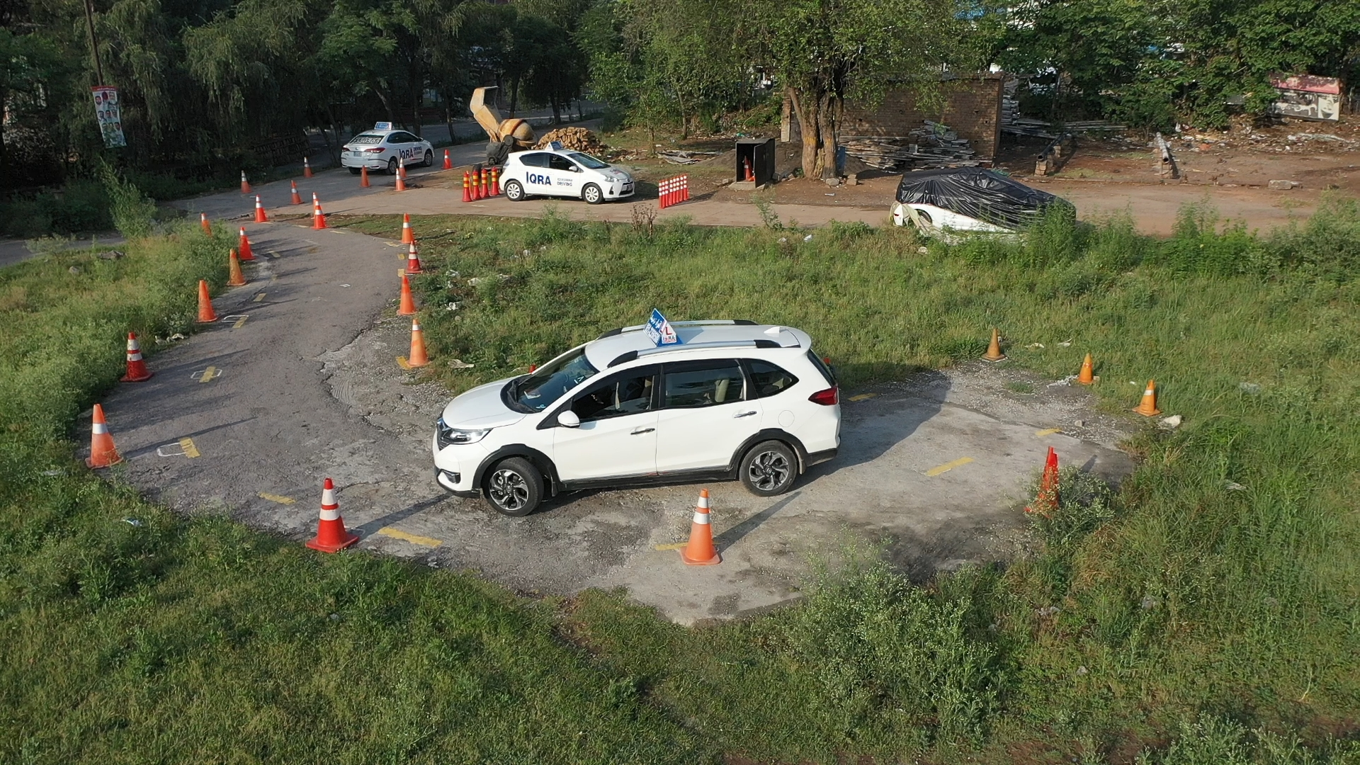 White SUV navigating a cone-marked driving course on a paved test track surrounded by grass, viewed from above
